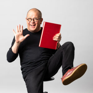 Le comédien tient un livre rouge dans sa main.