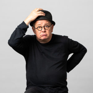 Le comédien semble étonné. Il porte un chapeau melon.