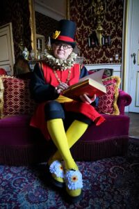 Le comédien porte un costume aux couleurs du drapeau belge. Il pose avec un livre dans les mains.