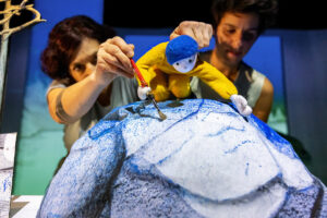 Une marionnette peint un rocher du décor.