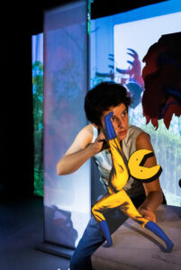 Le comédien manipule une marionnette qui ressemble à un super-héros astronaute.