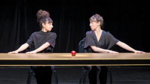 Les deux comédiennes sont assises et se toisent du regard.