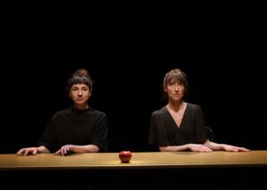 Les deux comédiennes sont assises derrière une table sur laquelle est posée une pomme.