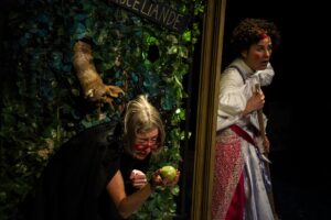 Les comédienne rejoue Blanche Neige : la sorcière tient la pomme devant Blanche Neige.