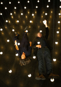 Les deux comédiens sont allongés sous des ampoules suspendues.