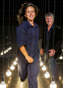 La comédienne marche entre deux lignes d'ampoules suspendues.