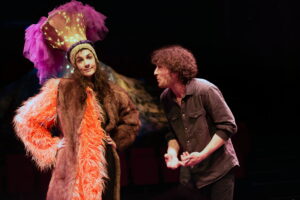 Les deux comédiens discutent, la comédienne porte un manteau de fourrure orange.