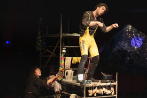 Le comédien est debout sur un échafaudage et porte un cycliste de vélo.