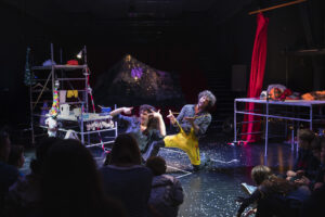 Le comédien est agenouillé au milieu de la scène et montre quelque chose au public.