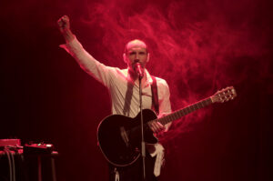 Le comédien chante, une guitare dans les mains.