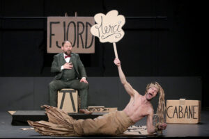 L'un des comédien est déguisé en sirène, avec une queue et des cheveux en carton.