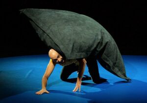 Le comédien porte un coussin géant sur son dos.