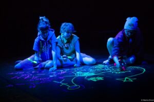 Les trois comédiennes font des dessins fluorescents au sol.