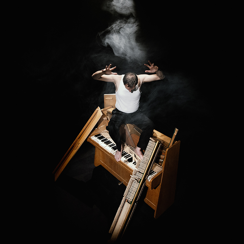 Le comédien est debout sur un piano droit cassé.