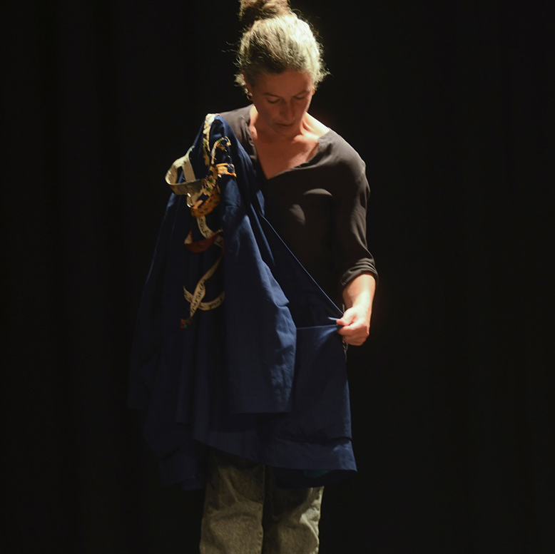 La comédienne tient dans ses mains un manteau avec des bouts de tissus accrochés.