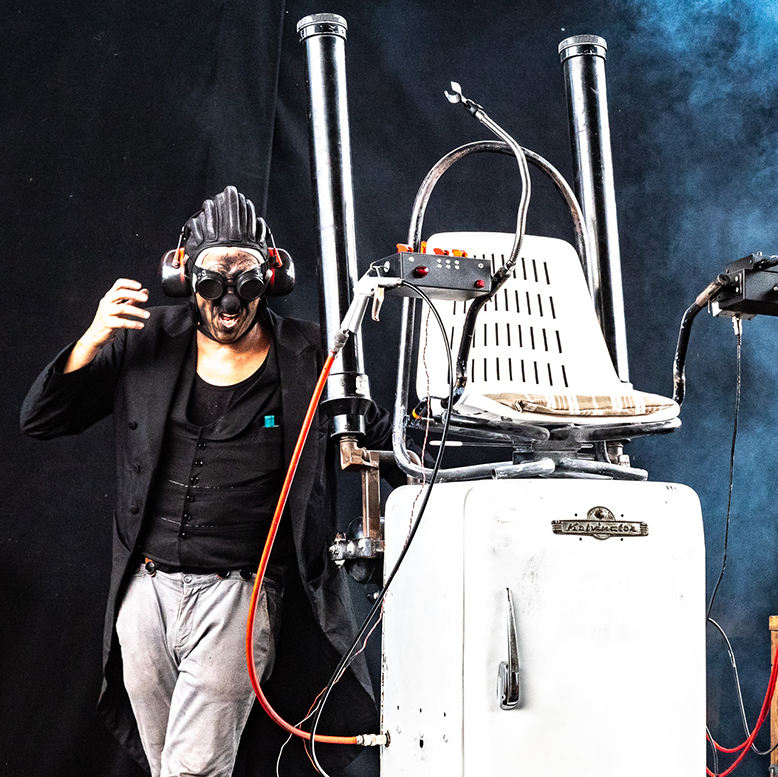 Le clown est à côté de son frigo sur lequel est installé un siège.