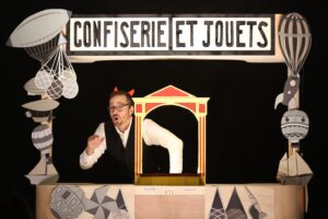 Le comédien est derrière son stand de confiseries et jouets.