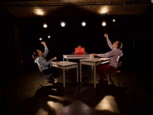 Deux circassiens lancent des balles en l'air, la troisième lit.