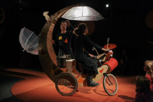 La comédienne est su un vélo trafiqué et tourne autour du comédien.