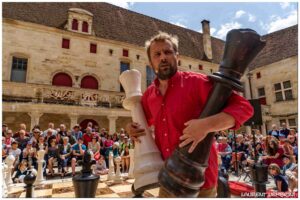 Le comédien tient deux grandes pièces d'échecs "reine".