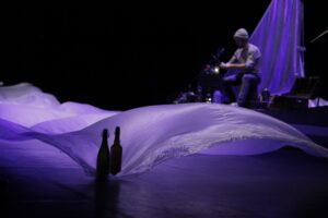 Un drap blanc bouge au sol avec de l'air, un musicien en arrière plan.