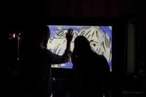 Les deux comédiens touchent un écran où est dessiné un visage.