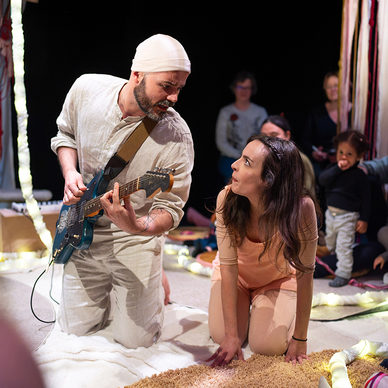 La comédienne et le musicien sont agenouillés au sol et se regardent.