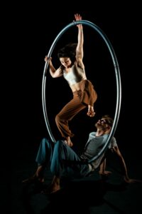 Le circassien tient la roue cyr, la circassienne est suspendue à la roue cyr.