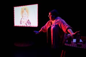 La comédienne écarte les bras, un écran en arrière plan avec un dessin de femme.