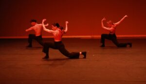 Les trois danseurs sont à moitié agenouillés au sol, les bras vers le ciel.