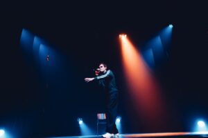 Le comédien chante sur scène, la main tendue vers le public.