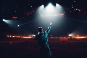 Le comédien est vu de dos, il tend le bras et le doigt vers public.